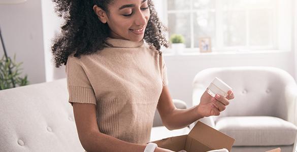 Young woman removes sample jar of cream from a marketing mail parcel.